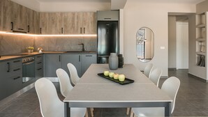 A modern kitchen with grey cabinets, a stainless steel refrigerator, and a dining table with four apples. - Luxury Living Suite-2 bedroom-Sea View/115m² (Argostoli)