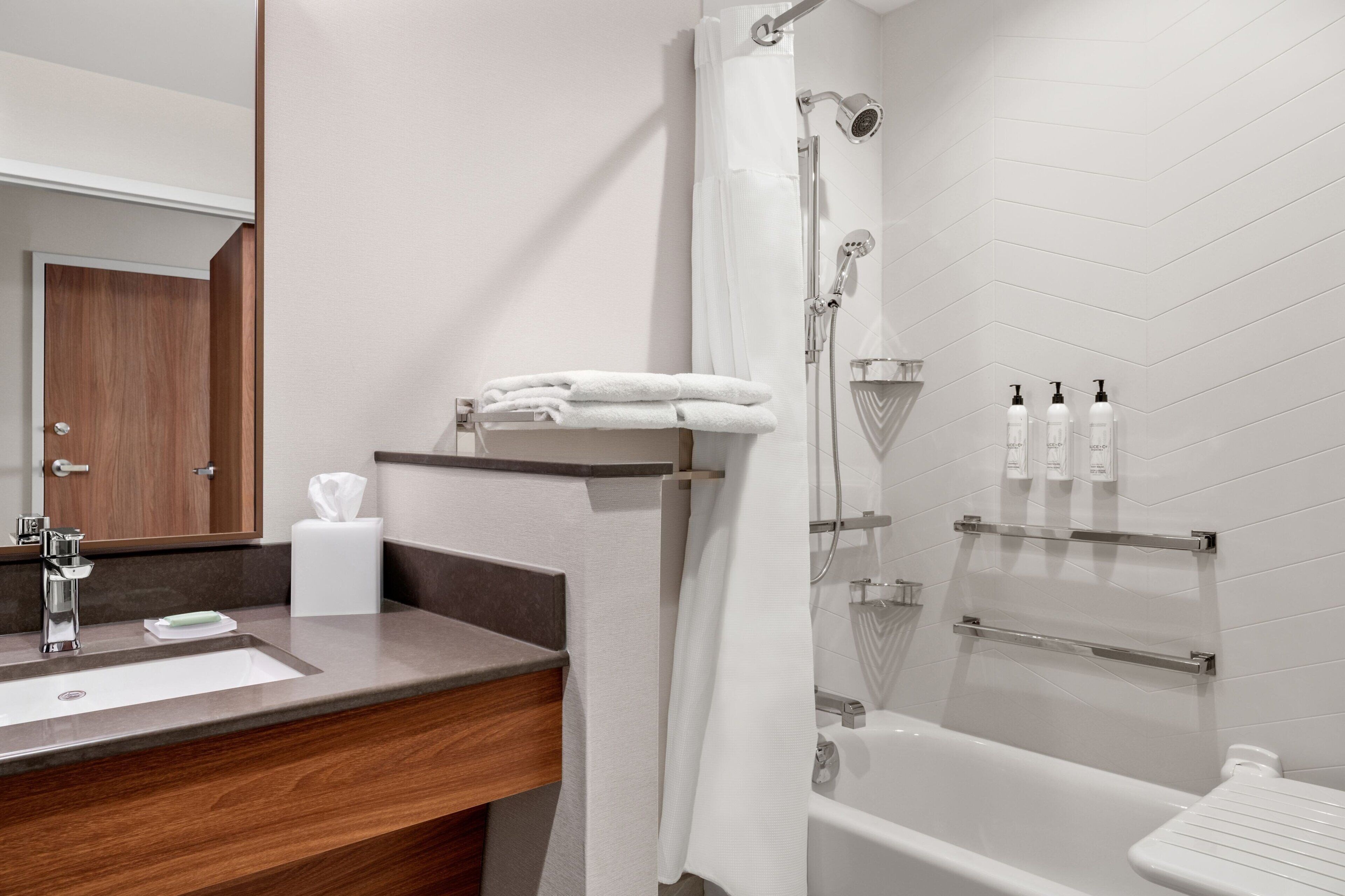 Une salle de bain moderne avec un meuble-lavabo en bois, un lavabo blanc, une douche avec une porte en verre et des articles de toilette rangés sur une étagère.
