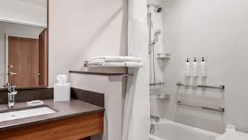 Ein modernes Badezimmer mit einem Holzbadezimmer-Möbelstück, einem weißen Waschbecken, einer Dusche mit Glastür und Pflegeprodukten auf einem Regal.