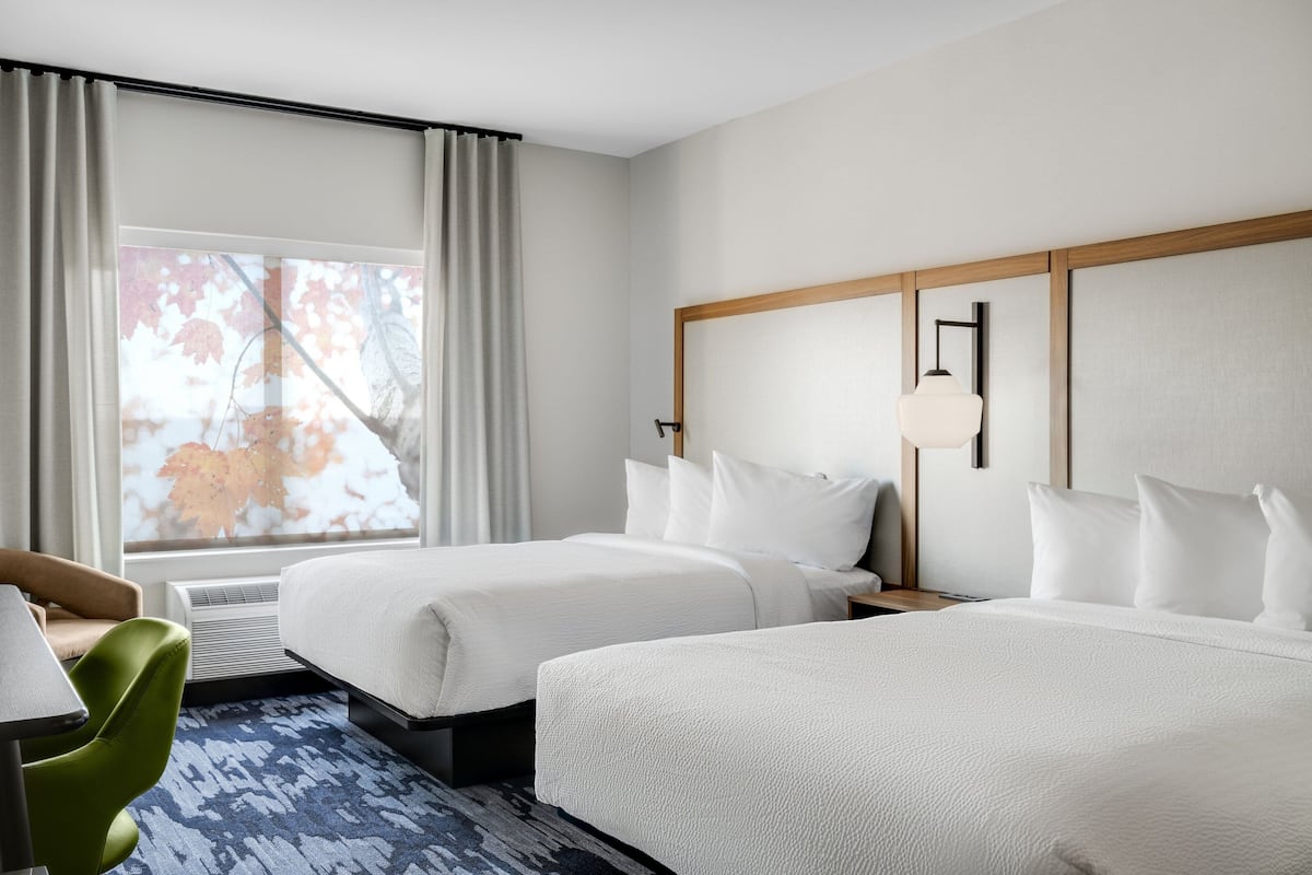 Een hotelkamer met twee bedden, een bureau, een stoel en een groot raam met gordijnen.