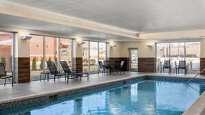 Une piscine intérieure dotée de chaises longues et de tables, de grandes fenêtres et offrant une vue sur l’extérieur.