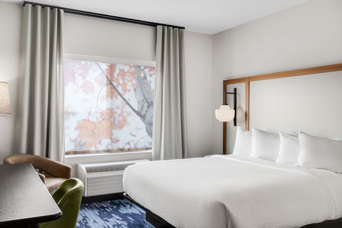 Hotelkamer met een groot bed, een bureau, een stoel, een raam met gordijnen en een wandlamp.