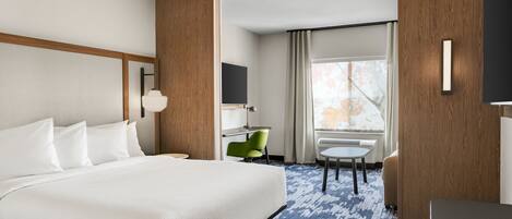 Ein Hotelzimmer mit einem großen Bett, einem Schreibtisch, einem Stuhl und einem Vorhangfenster.