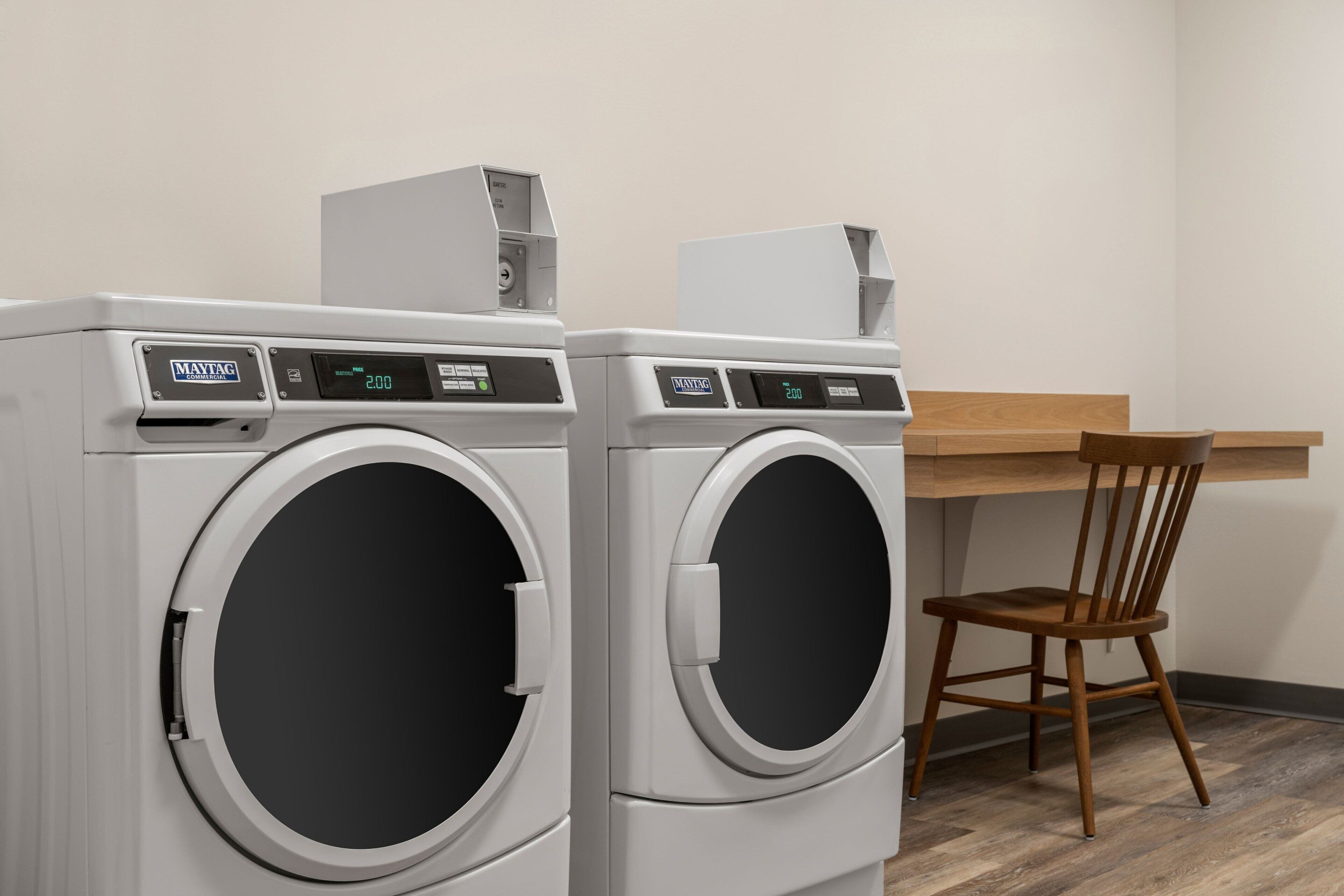 Two Maytag front-loading washing machines in a room with a wooden chair and a desk.