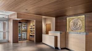 Un espace d’accueil avec un comptoir de réception en bois, une porte vitrée donnant accès à une pièce de rangement et un élément décoratif mural.