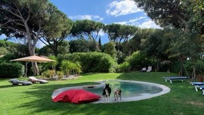 Un espace piscine avec des chaises longues et un parasol rouge.