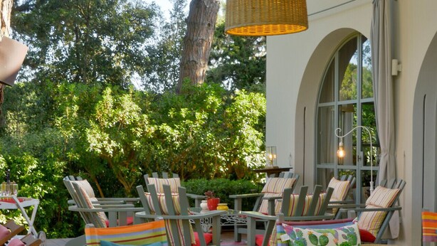 An outdoor patio area with multiple lounge chairs and tables, surrounded by greenery and a large tree. - Villa Gioconda - Homelike Villas (Bibbona)