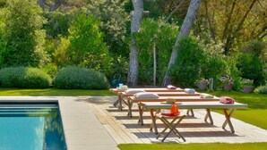 A poolside area with lounge chairs and a table, surrounded by lush greenery and trees. - Villa Gioconda - Homelike Villas (Bibbona)