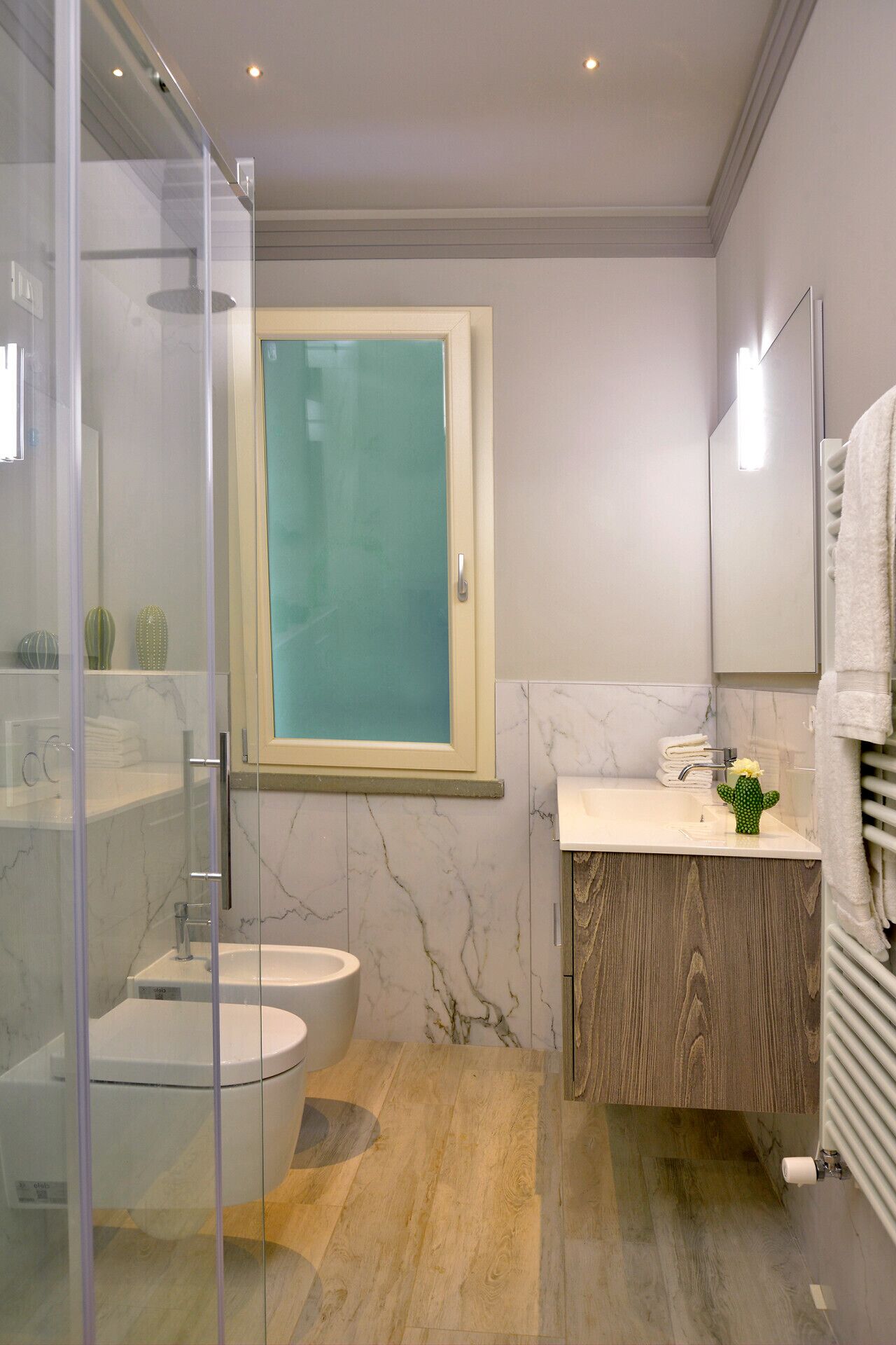 Un baño moderno con mampara de vidrio, inodoro, lavamanos con tocador de madera y espejo.