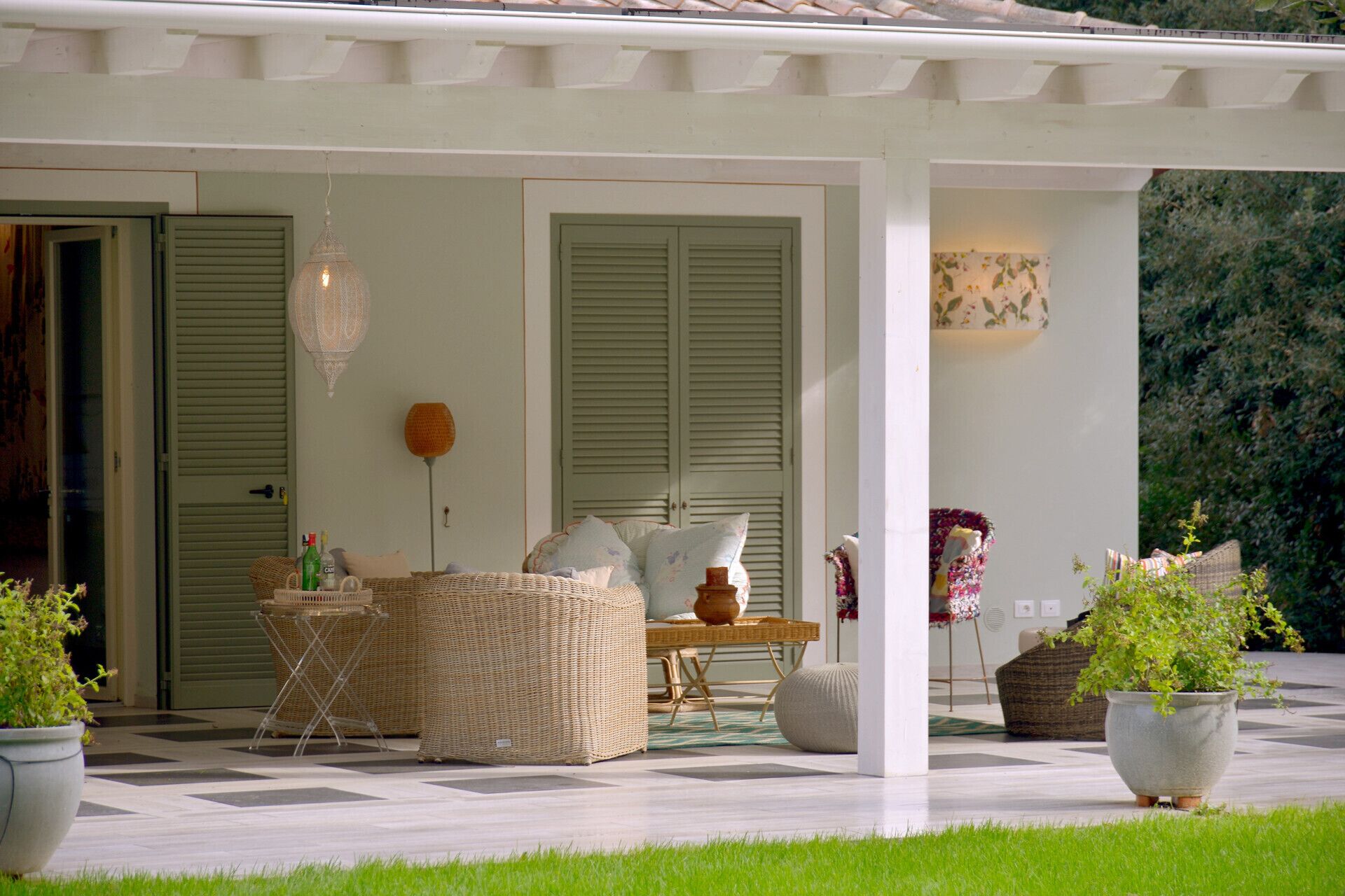 A covered outdoor seating area with wicker furniture, a table, and potted plants.