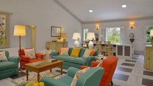 A spacious living room with a large sofa, a coffee table, and a dining area with chairs. There are multiple lamps and a mirror on the wall. - Villa Allegra - Homelike Villas (Bibbona)