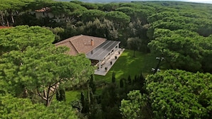 A building with a tiled roof, surrounded by dense green trees and a clear sky. - Villa Allegra - Homelike Villas (Bibbona)
