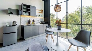 A modern kitchen with built-in appliances, a dining area with a round table and chairs, and large windows offering a view of greenery. - w* | Glorious Loft w/ Beautiful Deco in Roma Norte (Ciudad de México)