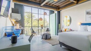 A modern hotel room with a large bed, a desk with a chair, a small table, and a large window offering a view of the outdoors. - w* | Glorious Loft w/ Beautiful Deco in Roma Norte (Ciudad de México)