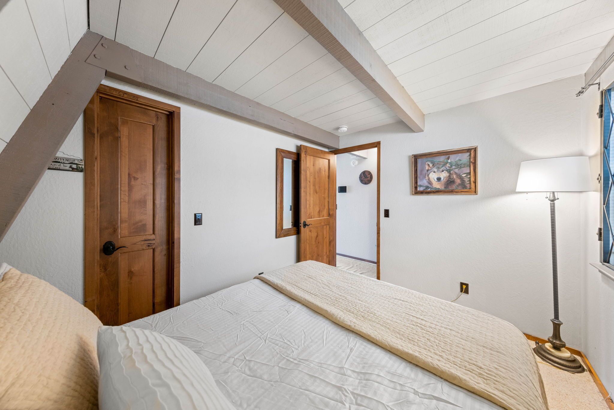 A bedroom with a bed, wooden doors, a mirror, a lamp, and a framed picture on the wall.
