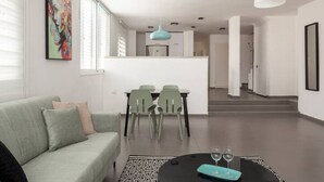 A modern living room with a sofa, a dining table with chairs, a pendant light, and a kitchen area in the background. - Amazing APT Bat-Yam Near Beach (Bat Yam)