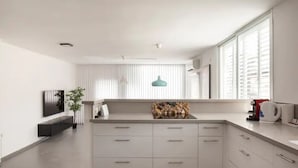 A modern kitchen with white cabinetry, a central island, a hanging light fixture, and a large window with blinds. - Amazing APT Bat-Yam Near Beach (Bat Yam)