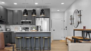 A modern kitchen with grey cabinets, stainless steel appliances, and a central island with stools. - Slabtown 203 Downtown Location with Two Balconies! (Traverse City)