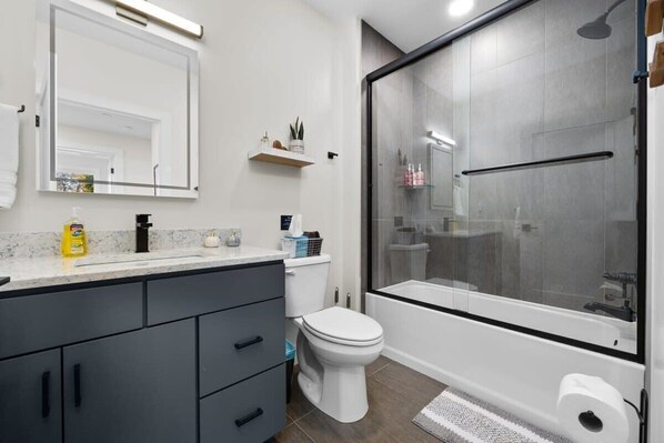 A modern bathroom with a glass-enclosed shower, a white toilet, and a vanity with a mirror and storage. - Slabtown 203 Downtown Location with Two Balconies! (Traverse City)