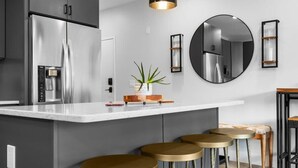A modern kitchen with a stainless steel refrigerator, a white countertop, and three gold stools. - Slabtown 203 Downtown Location with Two Balconies! (Traverse City)