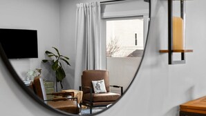 A modern living room with a large mirror, a brown leather armchair, a wooden coffee table, and a potted plant. - Slabtown 203 Downtown Location with Two Balconies! (Traverse City)