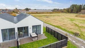 Una casa moderna con patio, jardín cercado y vistas a un paisaje rural.
