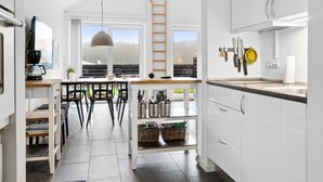Una cocina moderna con armarios blancos, un comedor con sillas negras y vistas al exterior a través de amplios ventanales.
