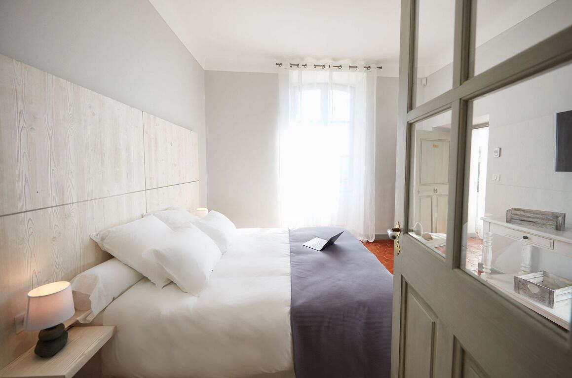 A hotel room with a bed, a nightstand with a lamp, a window with curtains, and a view of the outside.