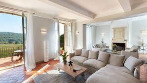 A spacious living room with a large sectional sofa, a wooden coffee table, and a view of a vineyard through large sliding glass doors. - Authentique Bastide Provençale au Cœur des Vignes D'un Domaine (Carcès)