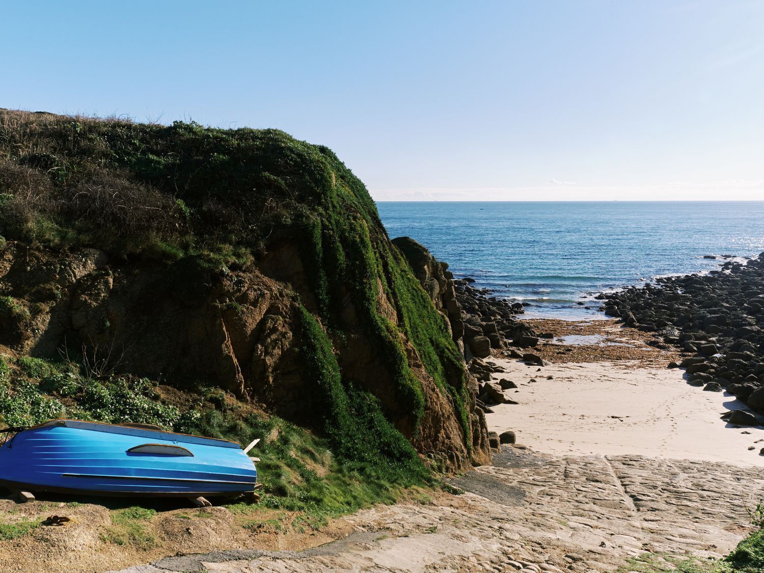 A beach with a kayak, rocky shoreline, and a clear view of the ocean.