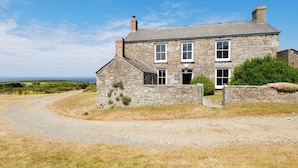 A stone house with a gravel driveway, a chimney, and a view of the sea. - Bosistow Farmhouse (Penzance)