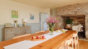 A dining area with a wooden table, a vase of flowers, and a stone fireplace. - Bosistow Farmhouse (Penzance)
