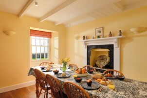 A dining room with a table set for breakfast, featuring bread, fruits, and beverages.