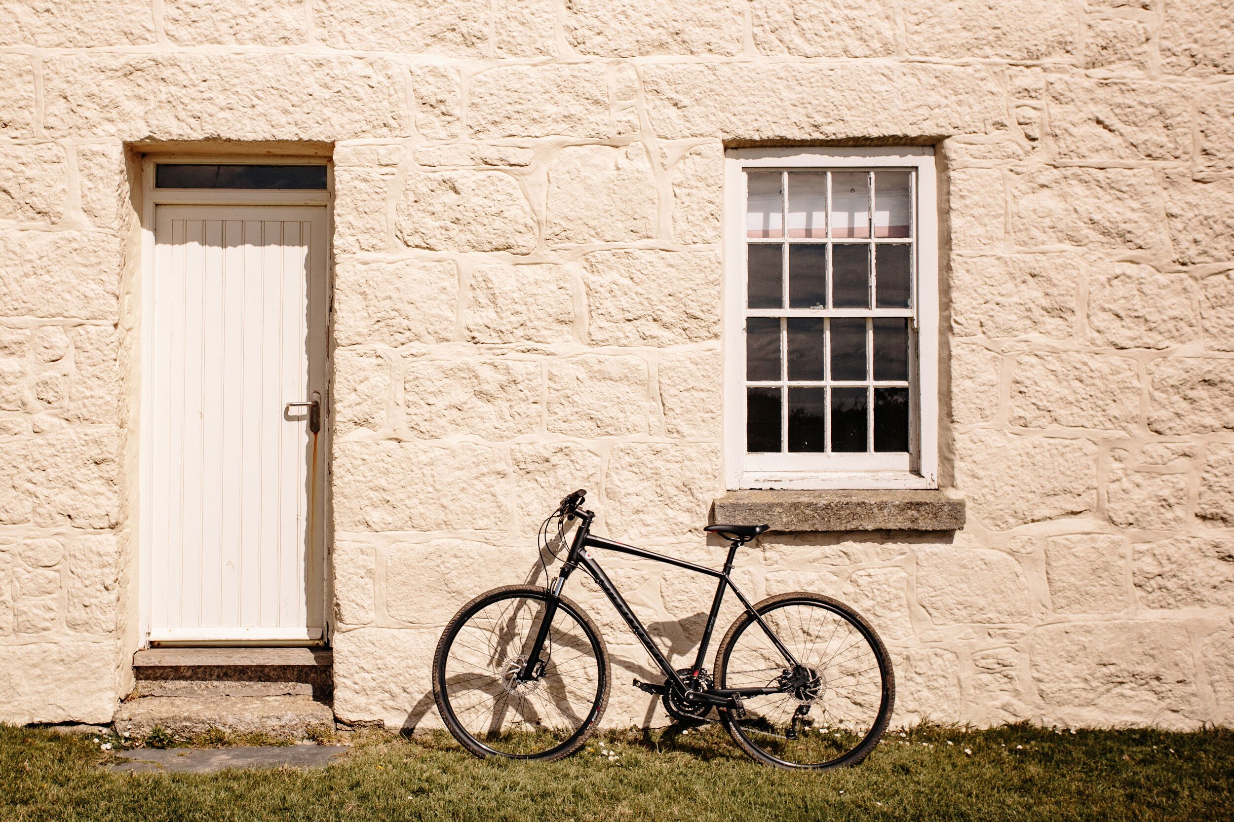 Uma bicicleta encostada em um edifício de pedra com uma porta branca e uma janela.