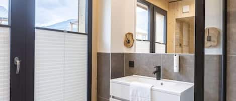 Un baño moderno con un ventanal grande, un lavabo blanco y un espejo.