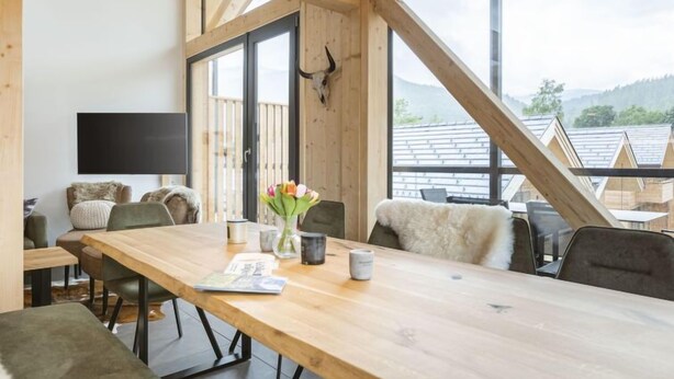 A modern interior with a long wooden table, comfortable seating, a flat-screen TV, and a large window with a mountain view. - #4a mit Sauna & Pool by Interhome (Sankt Georgen am Kreischberg)