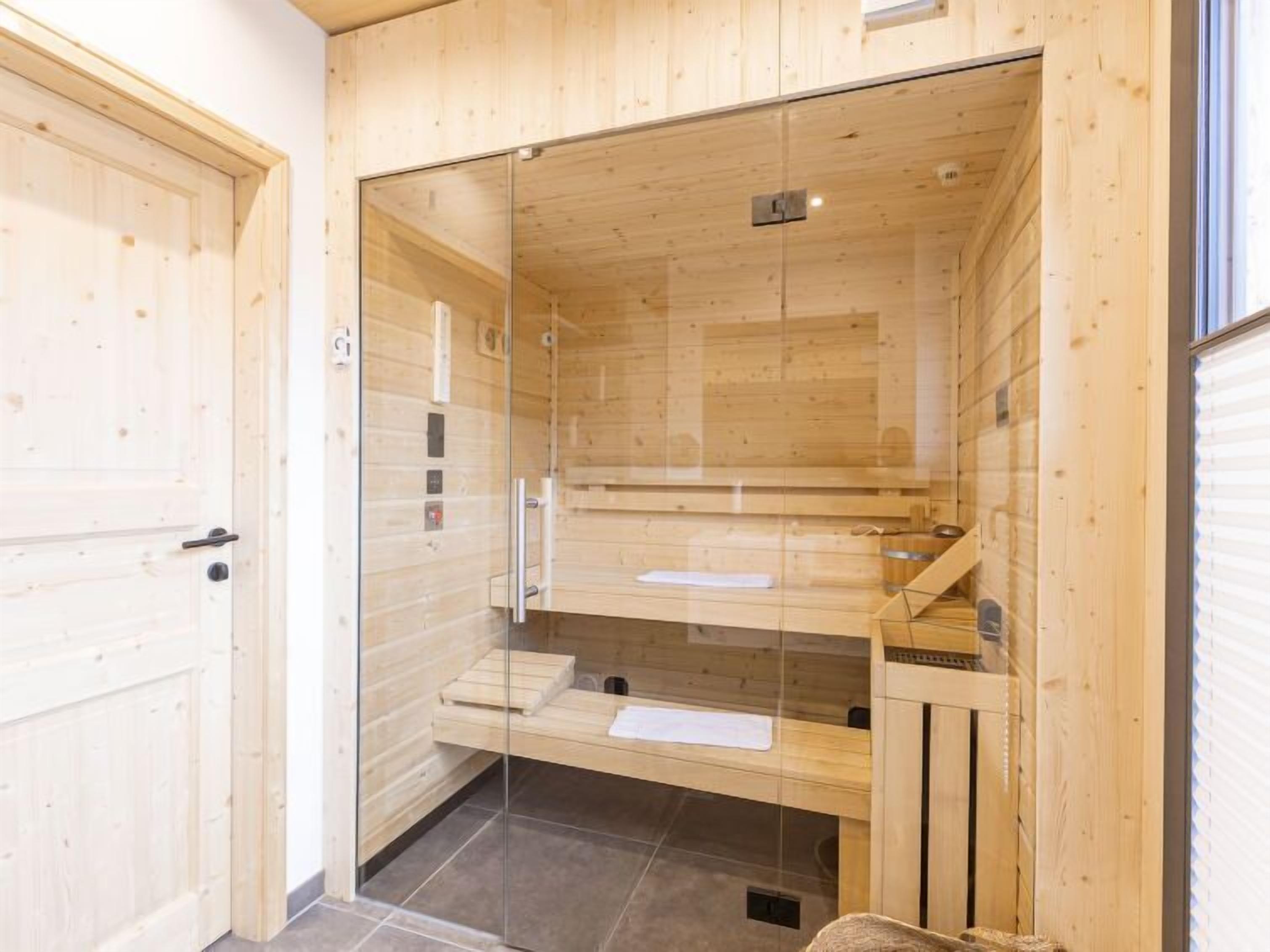 Een sauna met houten wanden en een glazen deur, met banken en een kleintje tafeltje.