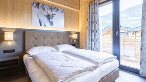A bedroom with a large bed, wooden walls, a mounted picture of a deer, and a view of a snowy landscape through a glass door. - #4a mit Sauna & Pool by Interhome (Sankt Georgen am Kreischberg)