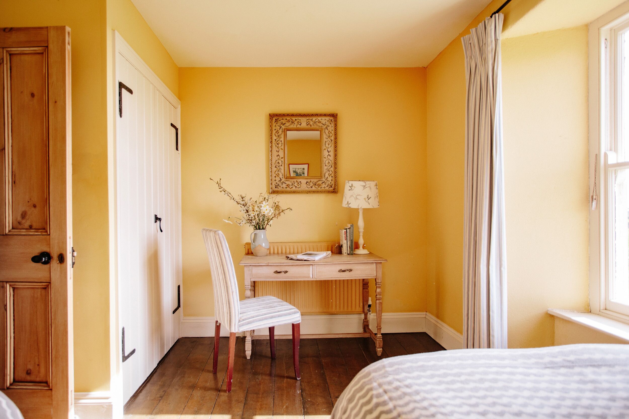 A room with a wooden desk, a chair, a bed, and a window with curtains.