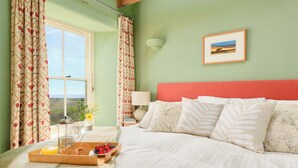 A bedroom with a bed, a tray of breakfast, a window, curtains, and a wall-mounted picture. - Higher Roskestal (Penzance)