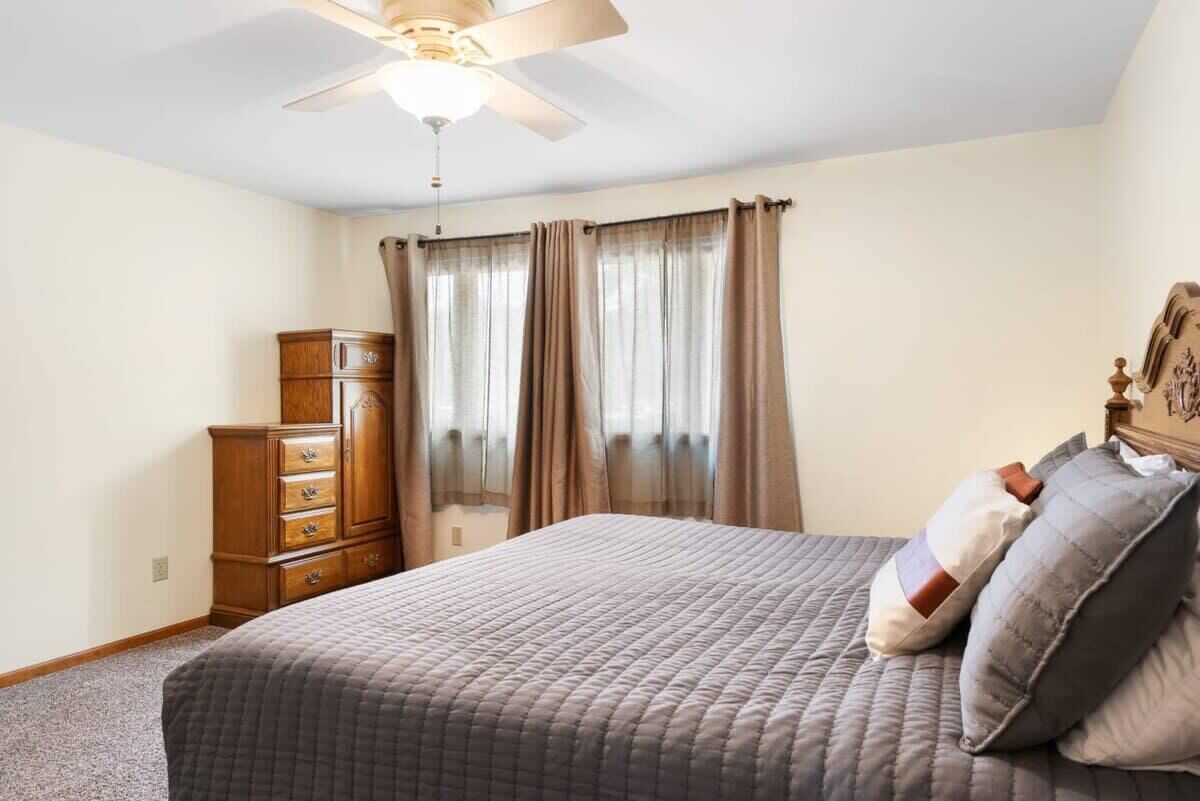 A bedroom with a bed, a ceiling fan, a dresser, and a window with curtains.
