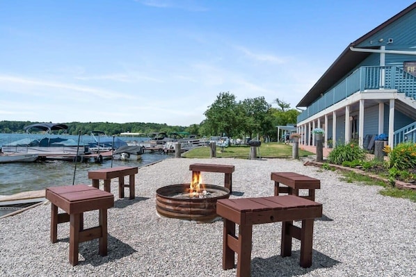 Un patio junto al lago con una fogata, asientos y un edificio con balcón.