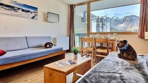 A cozy room with a sofa, a dining table, and a view of a mountainous landscape through a large window.