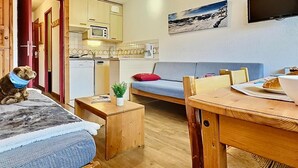 A cozy room with a bed, a sofa, a dining table, and a kitchenette.