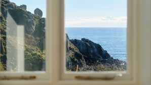 A coastal view through a window with rocky terrain and the sea. - Pendower Cottage (Penzance)