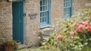 A stone cottage with a teal door and windows, a bench outside, and a sign reading "LOVE COTTAGE." - Cove Cottage (Penzance)