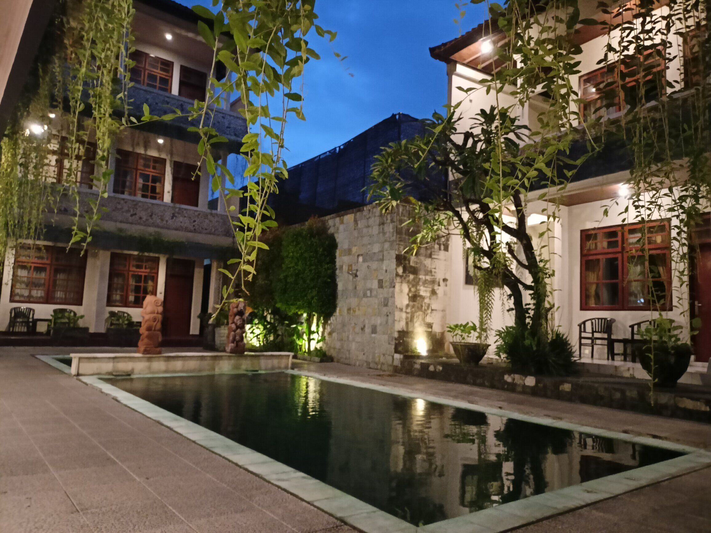 Un patio con piscina, paredes de piedra y plantas colgantes.