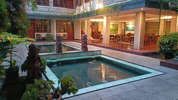 A courtyard with a pool, stone statues, and indoor seating areas.