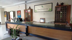 Zona de recepción con mostrador de madera, vitrina de vidrio y cartel de bienvenida enmarcado para Hotel Catur Aji Putra.