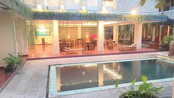 Ein Innenhof mit Pool, Sitzgelegenheiten im Freien und einem Gebäude mit großen Fenstern und Zierelementen.